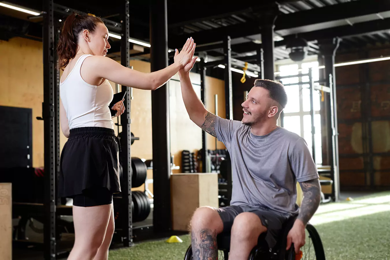 A disabled man in his wheel chair gives high five to his trainer
